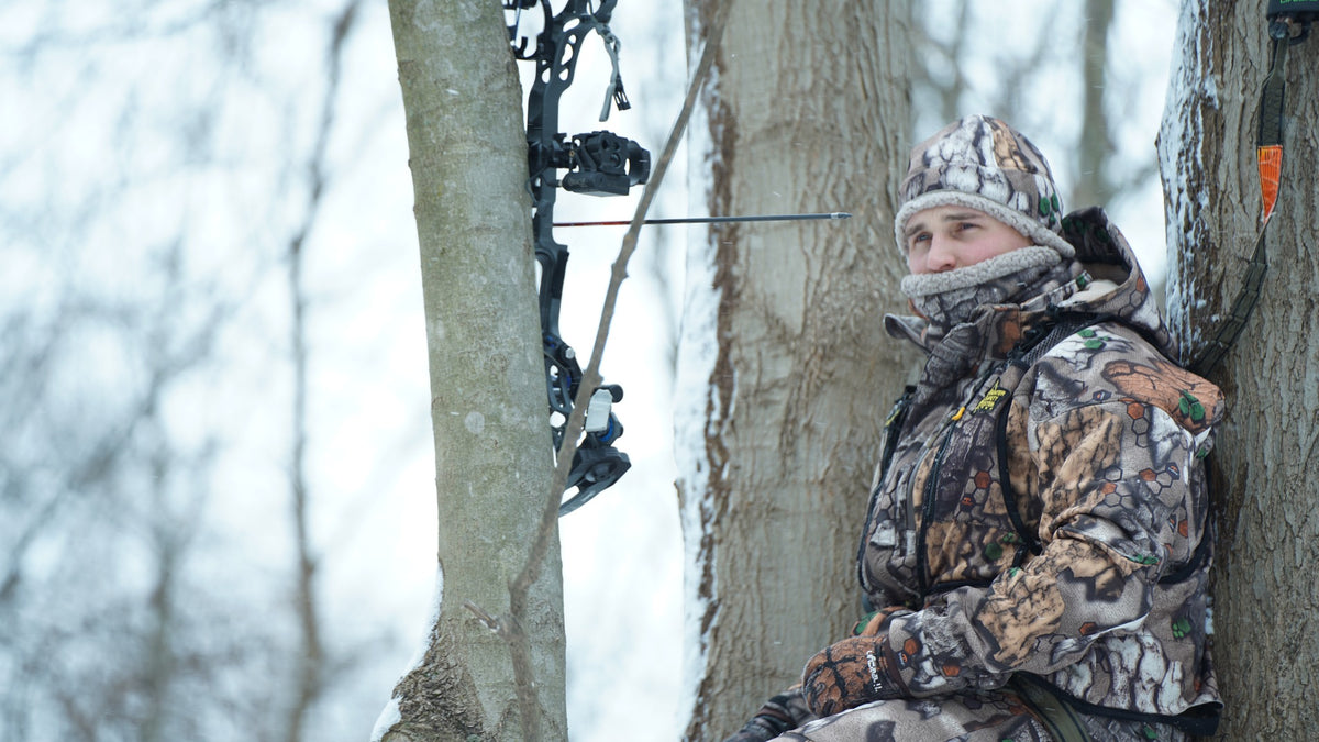 Hunter wearing an Impizi Parka, Beanie and Gaiter while waiting in a snowy tree stand